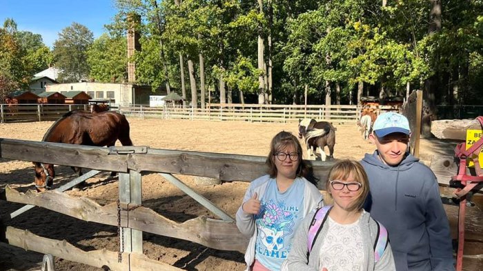 Uczniowie pozują do zdjęcia przy zagrodzie z koniami.