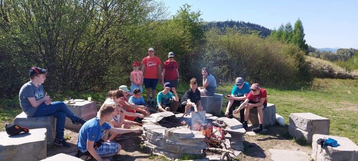 Uczniowie palą ognisko i pieką kiełbasę.