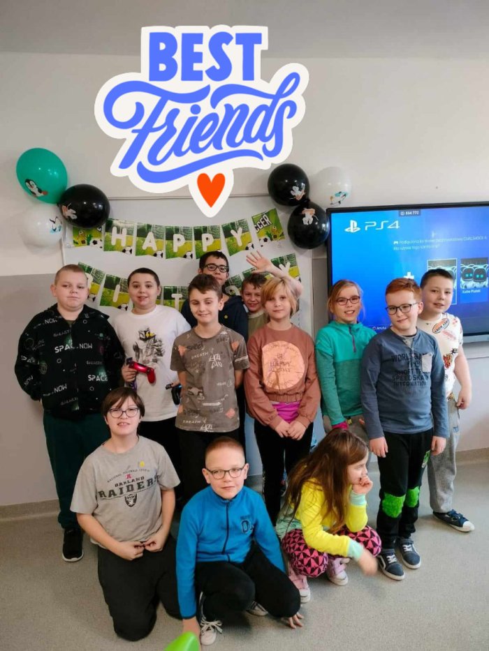 Uczniowie pozują do zdjęcia na tle dekoracji urodzinowej.