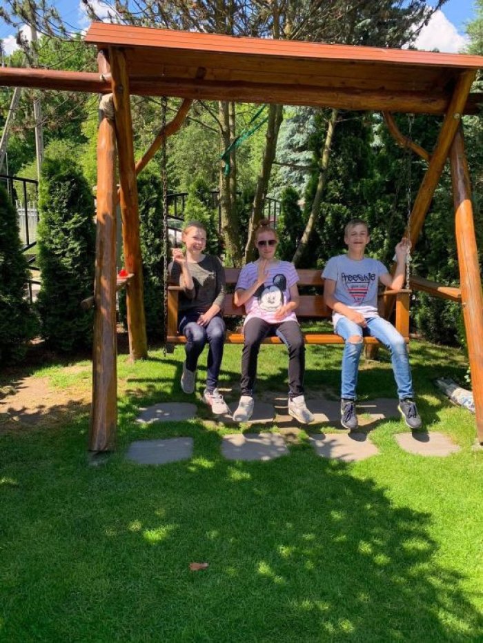 Uczniowie huśtają się na huśtawce w przydomowym ogródku.