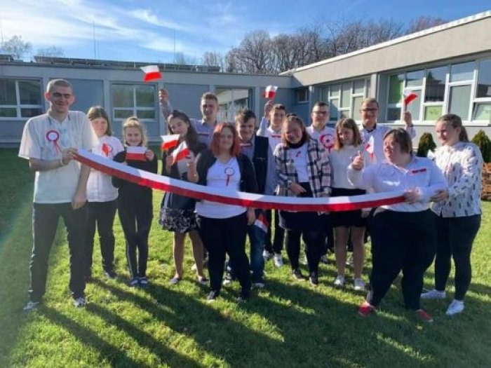 Uczniowie klas przysposabiających do pracy pozują do zdjęcia z flagą narodową.