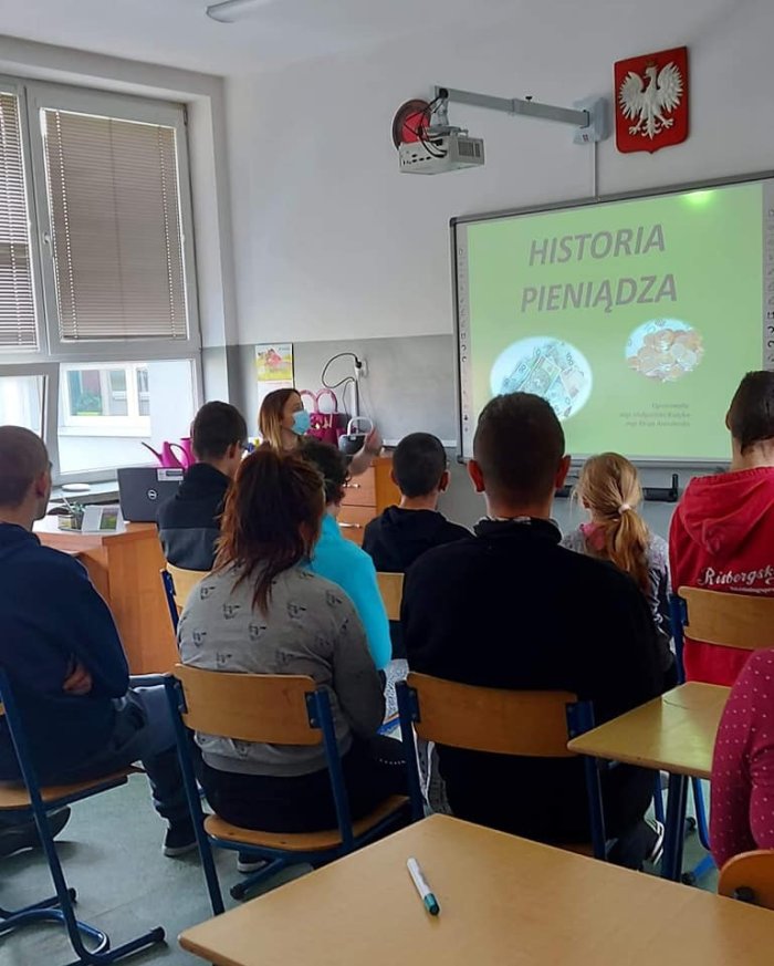 Uczniowie oglądają na tablicy multimedialnej prezentację o historii pieniądza