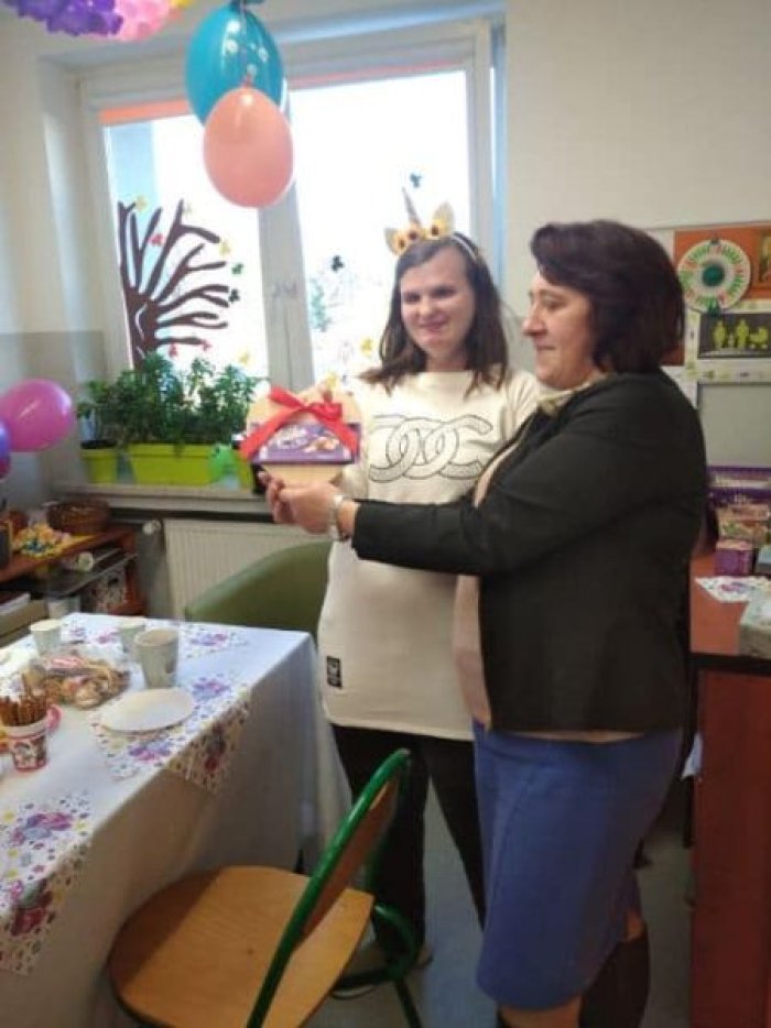 Nauczycielka wręcza prezent imieninowy uczennicy Kasi.
