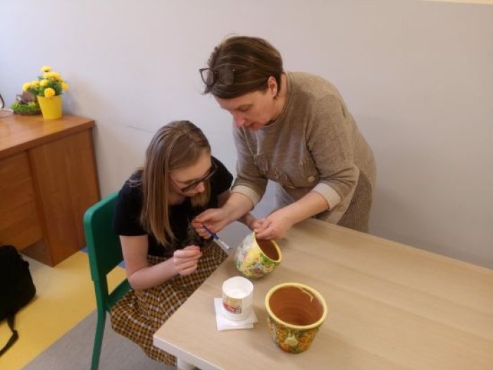 Wychowanka internatu pod opieką nauczyciela ozdabia doniczkę techniką decoupage.