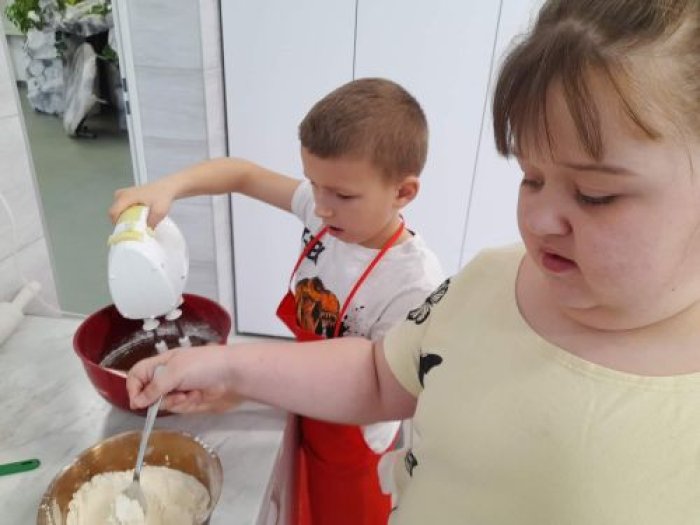 Uczennica miesza za pomocą łyżki mąkę na ciasto, a uczeń miksuje jajka.